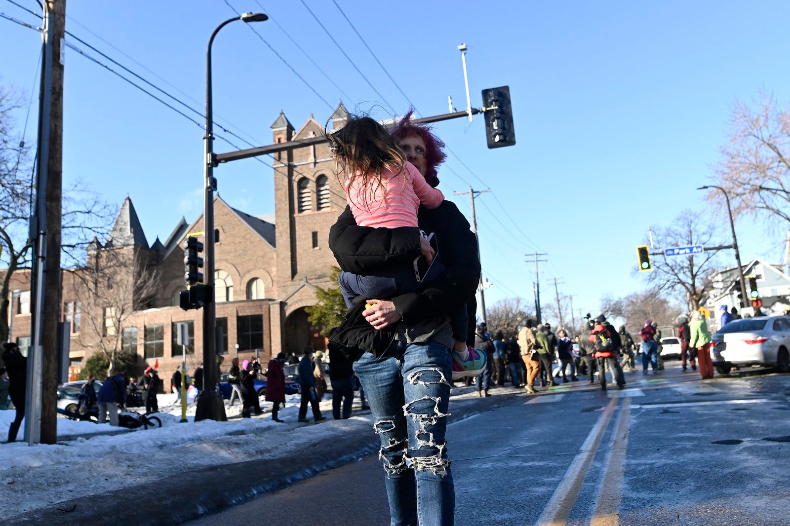 A person carries a child away from an intersection where ICE agents are being confronted by protesters.
