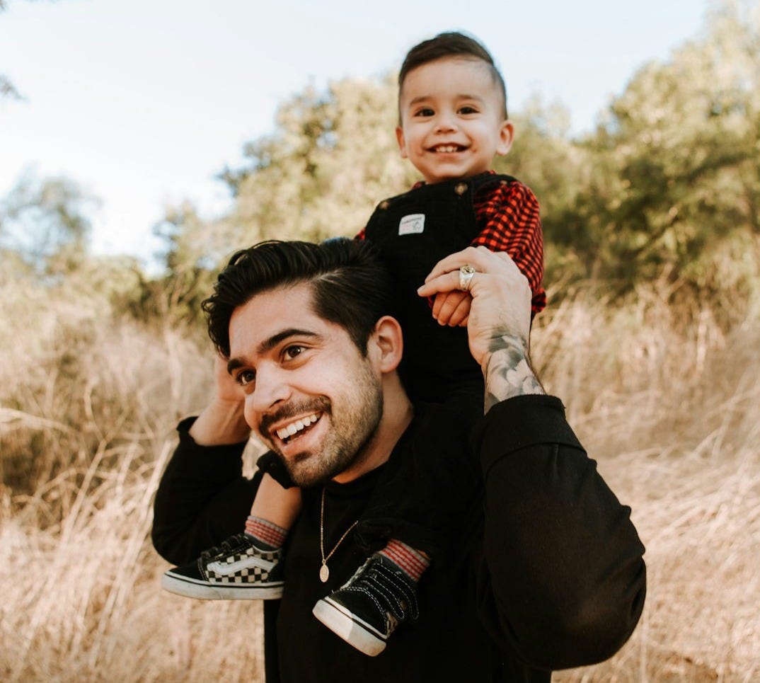 man in black jacket carrying baby in red and white checkered shirt during daytime