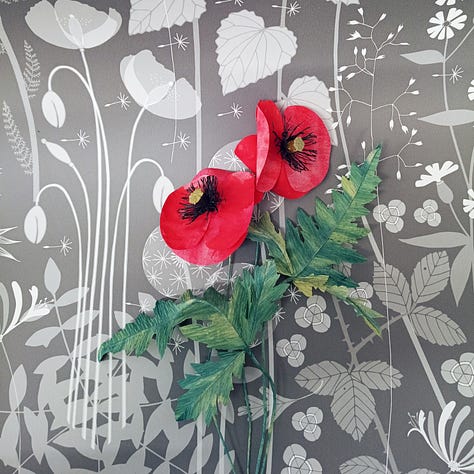 Brightly coloured paper flowers photographed against a backdrop of elegant, hedgerow inspired wallpapers.