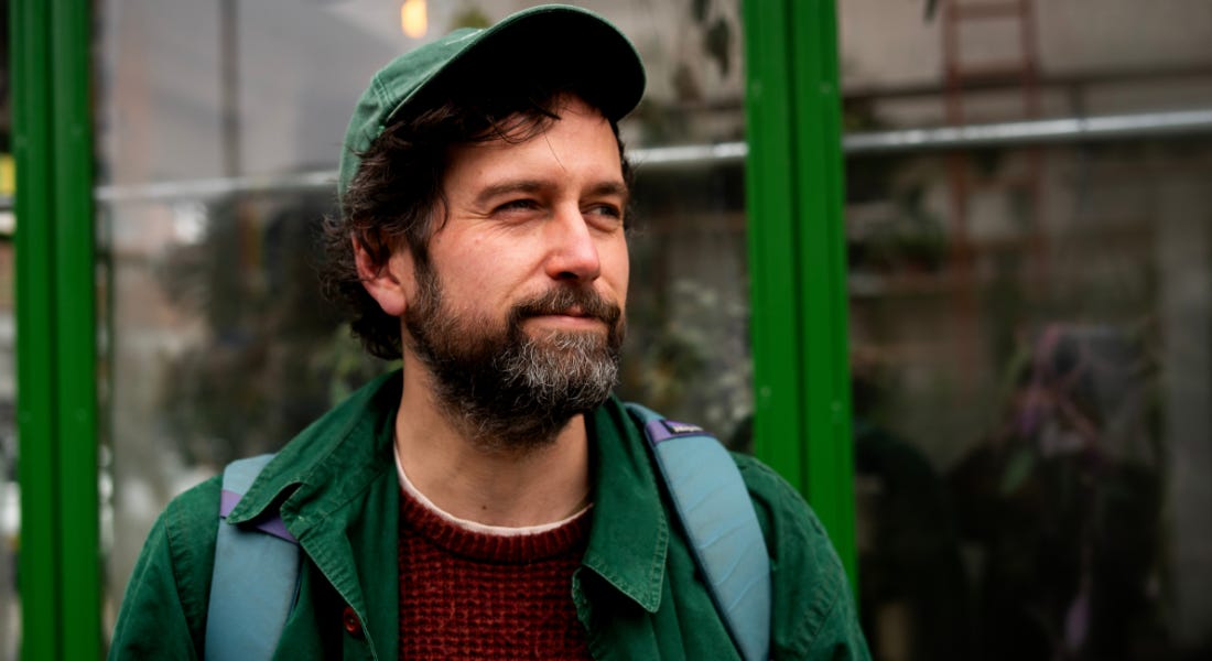 A picture of Adam Pickering - a man wearing a green cap and shirt standing in front of a shop front with green frames A picture of Adam Pickering - a man wearing a green cap and shirt standing in front of a shop front with green frames