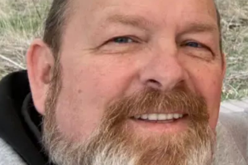 A closeup shot of an upper middle-aged white man with short-cropped graying brown hair looking up at the camera in a casual setting.