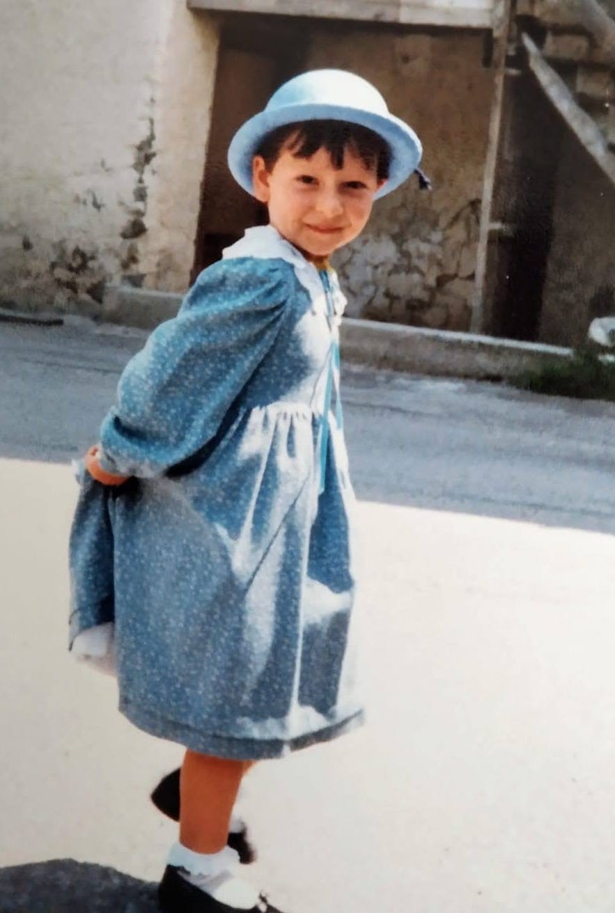 Bambina vestita di azzurro, con i capelli corti e un cappello sempre azzurro. Guarda in camera con un mezzo sorriso. Bambina vestita di azzurro, con i capelli corti e un cappello sempre azzurro. Guarda in camera con un mezzo sorriso.