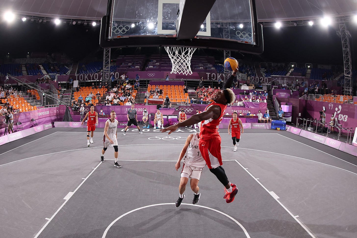 A player in a red jersey dunks over a player in a white jersey.