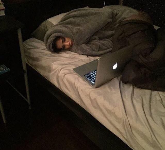 This may contain: a man laying in bed with his head on the pillow while looking at an apple laptop