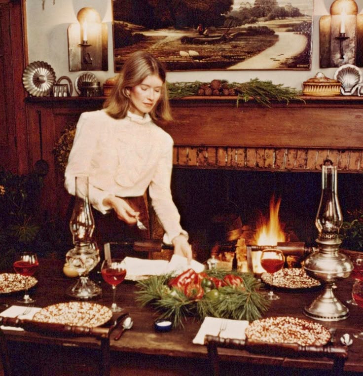This may contain: a woman standing in front of a fire place with food on the table next to her