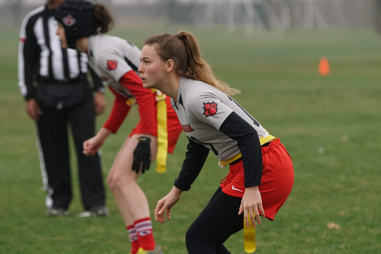 Two defensive women's flag football players in grey and red Canadian uniforms stand ready for a play. Two defensive women's flag football players in grey and red Canadian uniforms stand ready for a play.