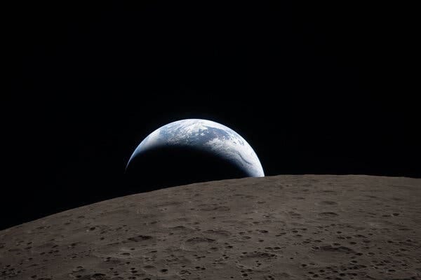 A view of a crescent Earth rising over the surface of the moon.