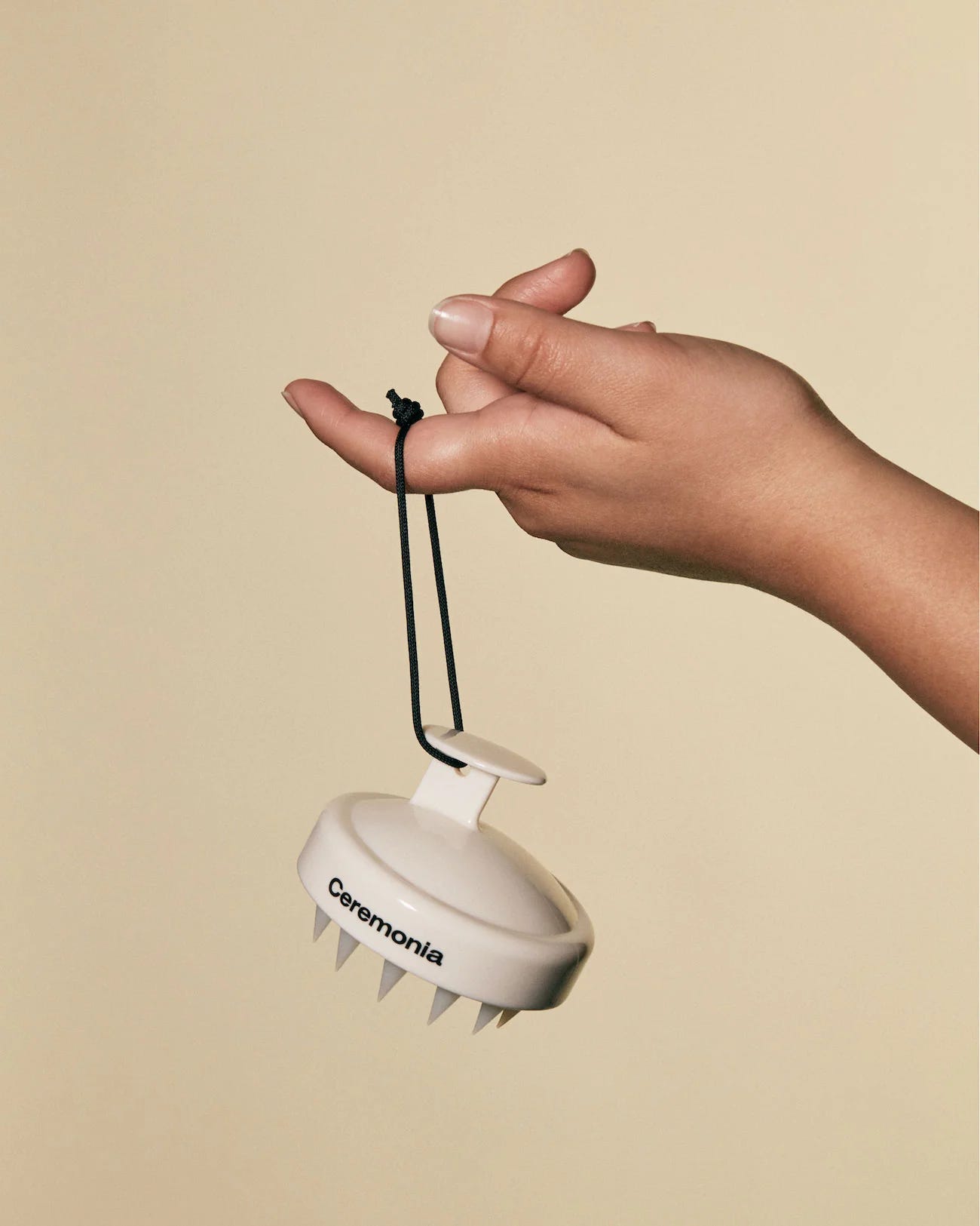 Hand holding the string of a scalp massager by one finger