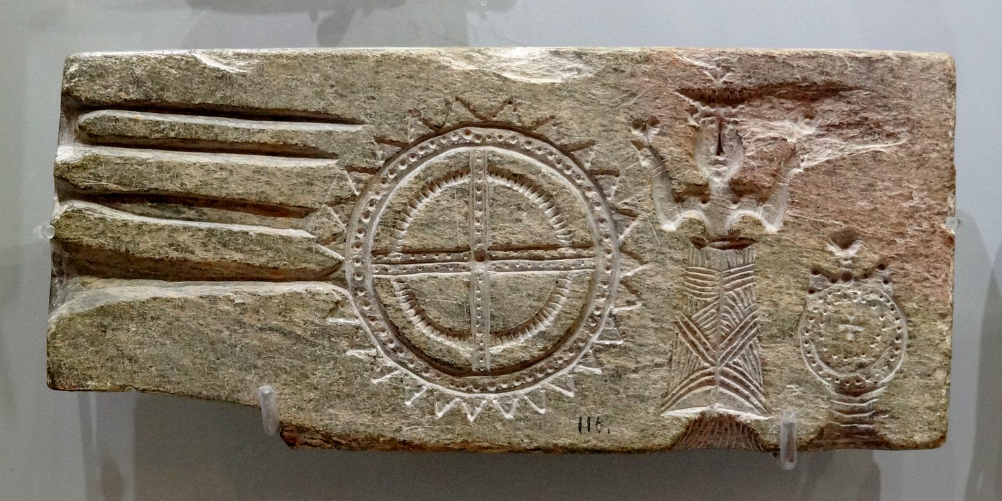Pale buff colored rectangular schist stone mold for metal casting found near Hagia Triada on the road from Palaikastro to Siteia, dated to 1370-1200 BCE. The mold includes several horizontal slots along the left side, a compass-like shape with triangular points around the edge in the center, and a female figure on the right.