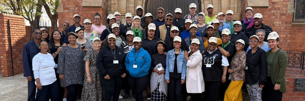 Group photo of people standing outside Kimberley Cathedral, all wearing matching white caps and smiling
