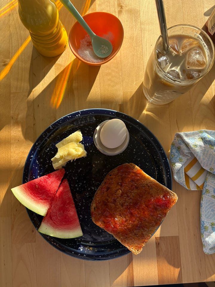 Two breakfast plates featuring a boiled egg, toast with jam, fresh fruit (watermelon in one, strawberries in the other) and pieces of cheese (cheddar in one, goats cheese in the other)