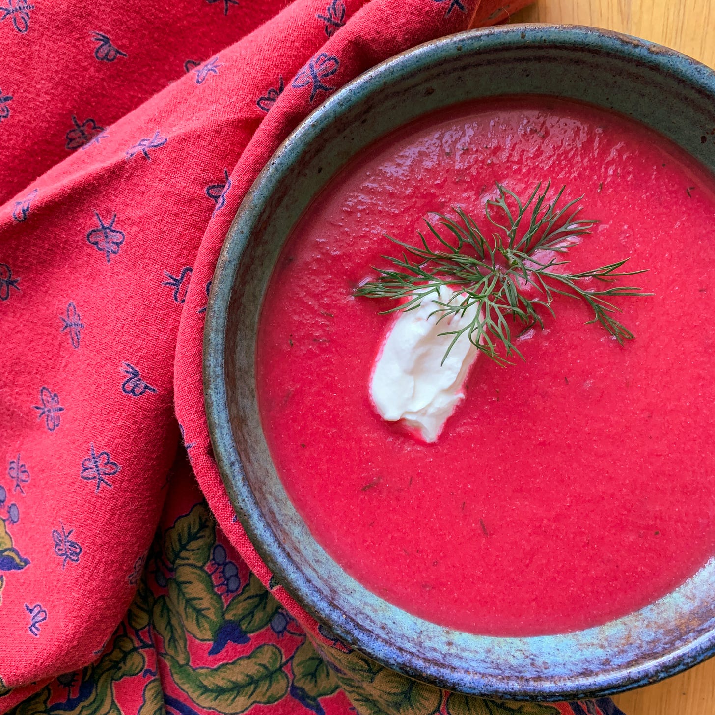 blue and green stoneware bowl filled with bright pink beet soup, topped with a dollop of sour cream and fresh dill sprigs