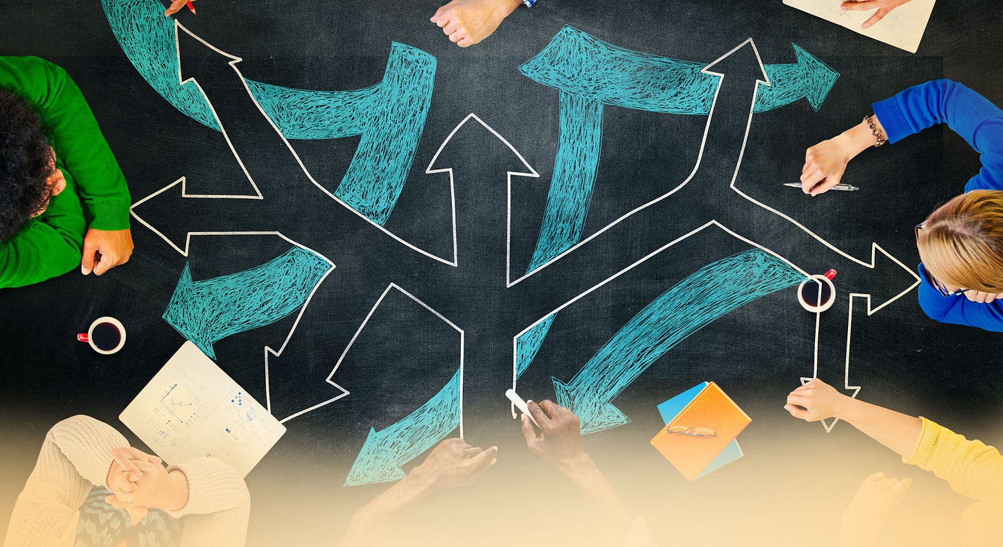 People sit at a table covered in chalk arrows representing different decisions or directions