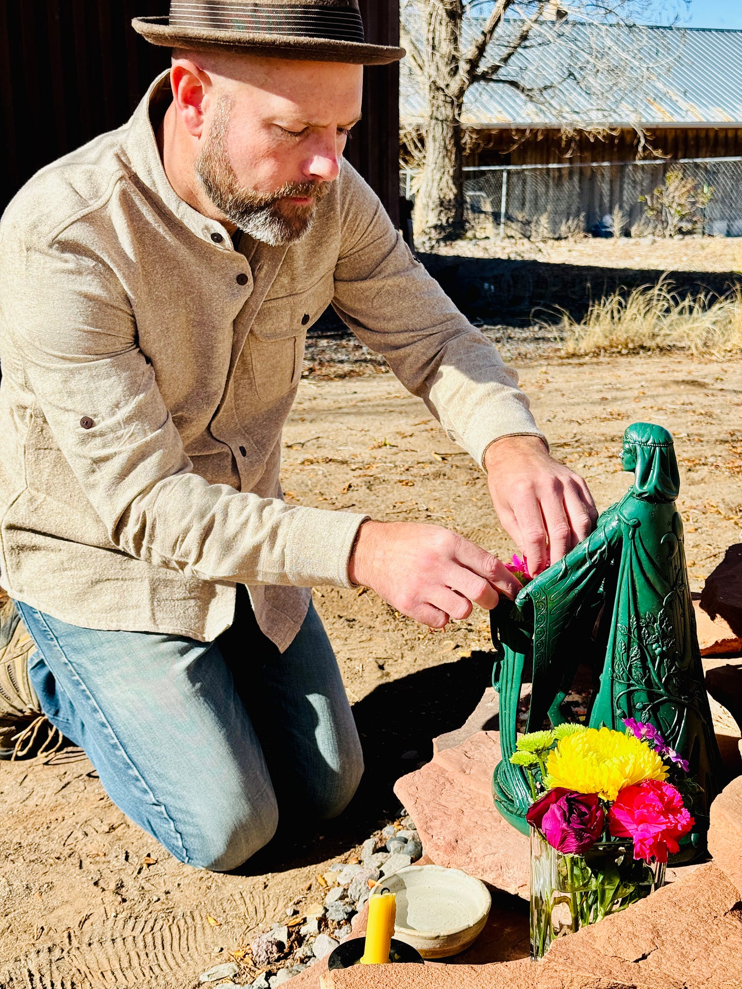 Ostara spring equinox ritual, person (the author) placing flowers at green goddess statue outdoors beside candle and offerings