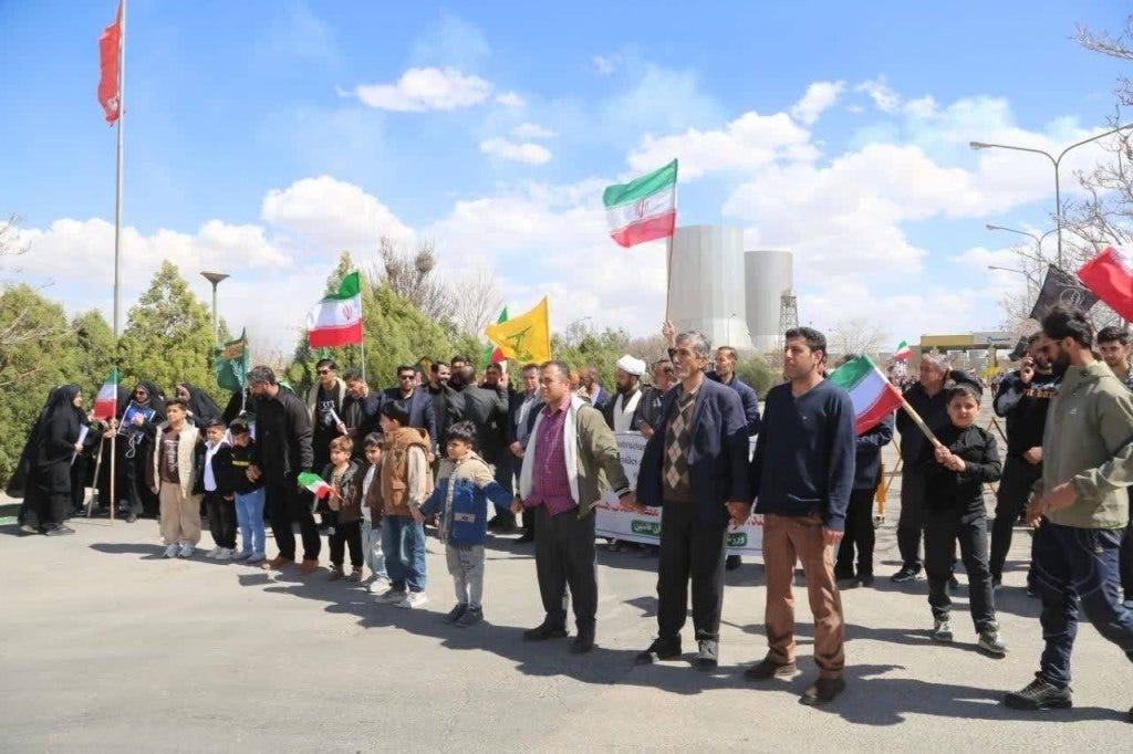 Iranian civilians forming human chains near a power plant, holding flags.