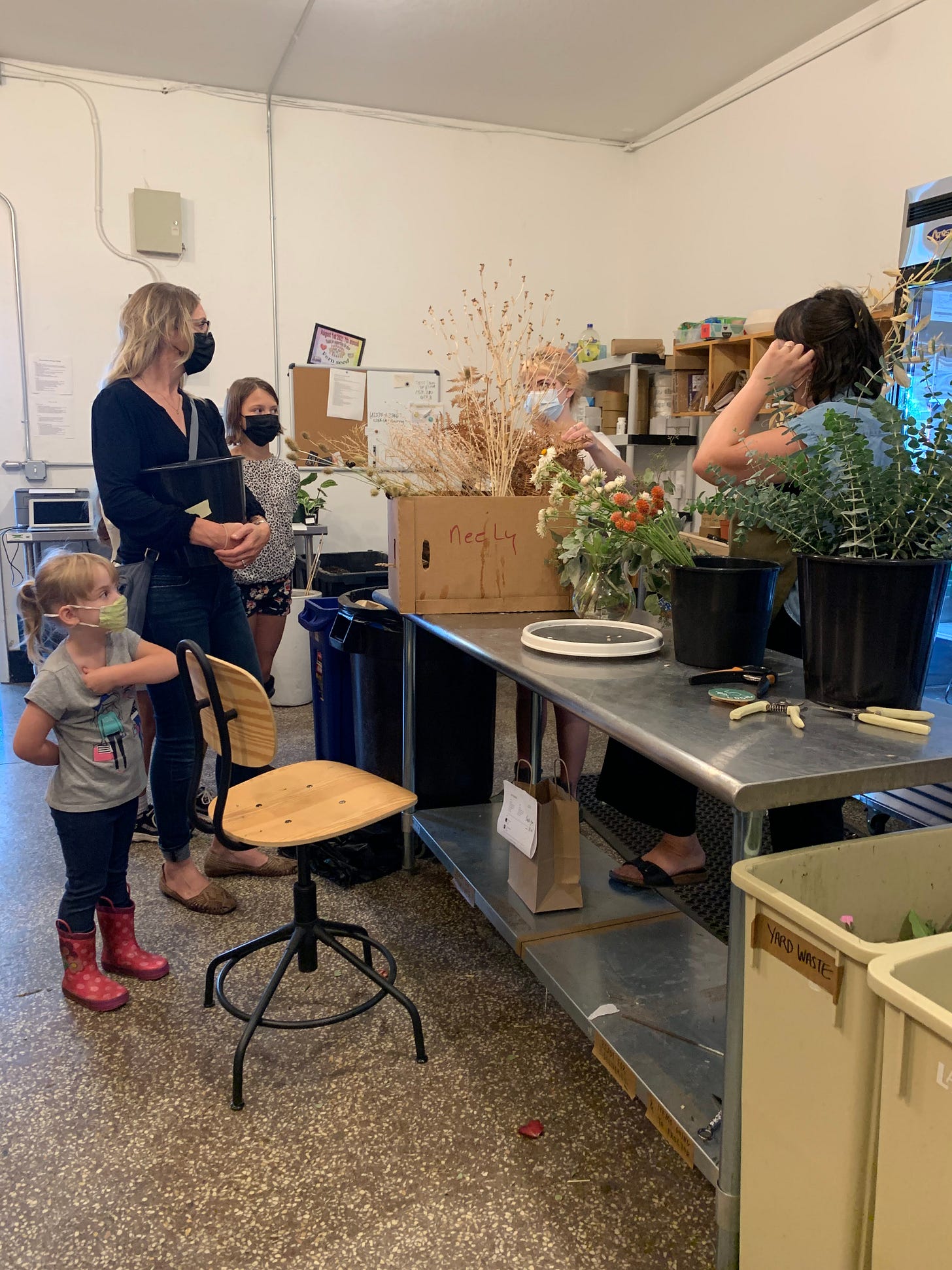 group of people standing around a steel work table with boxes and buckets of flowers group of people standing around a steel work table with boxes and buckets of flowers