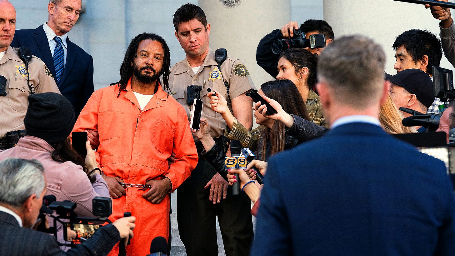 Elijah Stone in an orange jumpsuit surrounded by reporters facing Wesley Evers, back to camera, from The Rookie