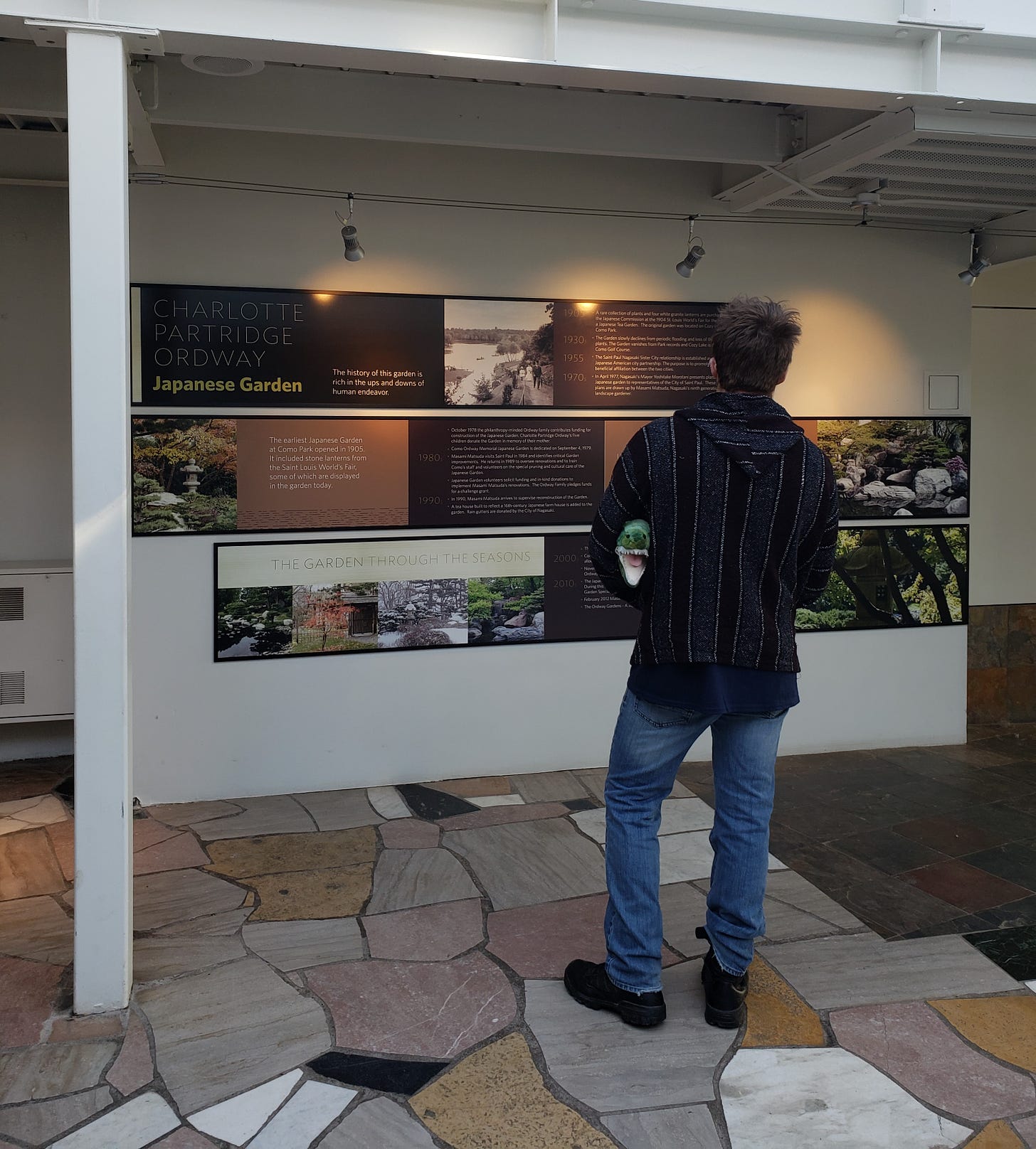 A person stands in front of a wall of placards reading about the Charlotte Partridge Ordway Japanese Garden. A person stands in front of a wall of placards reading about the Charlotte Partridge Ordway Japanese Garden.
