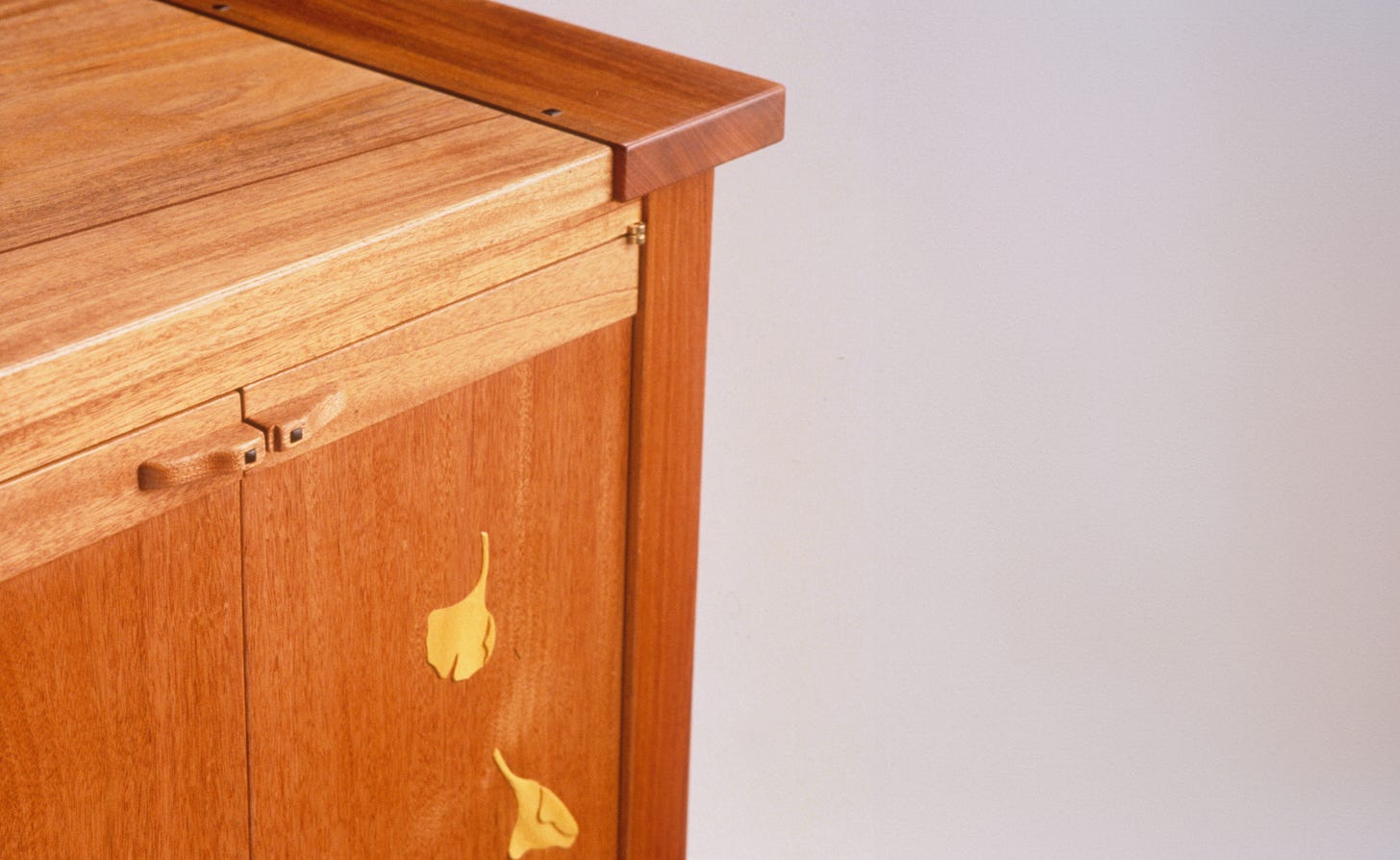 Detail of a handcrafted wooden sideboard featuring smooth joinery and delicate leaf-shaped inlays on the door panels.