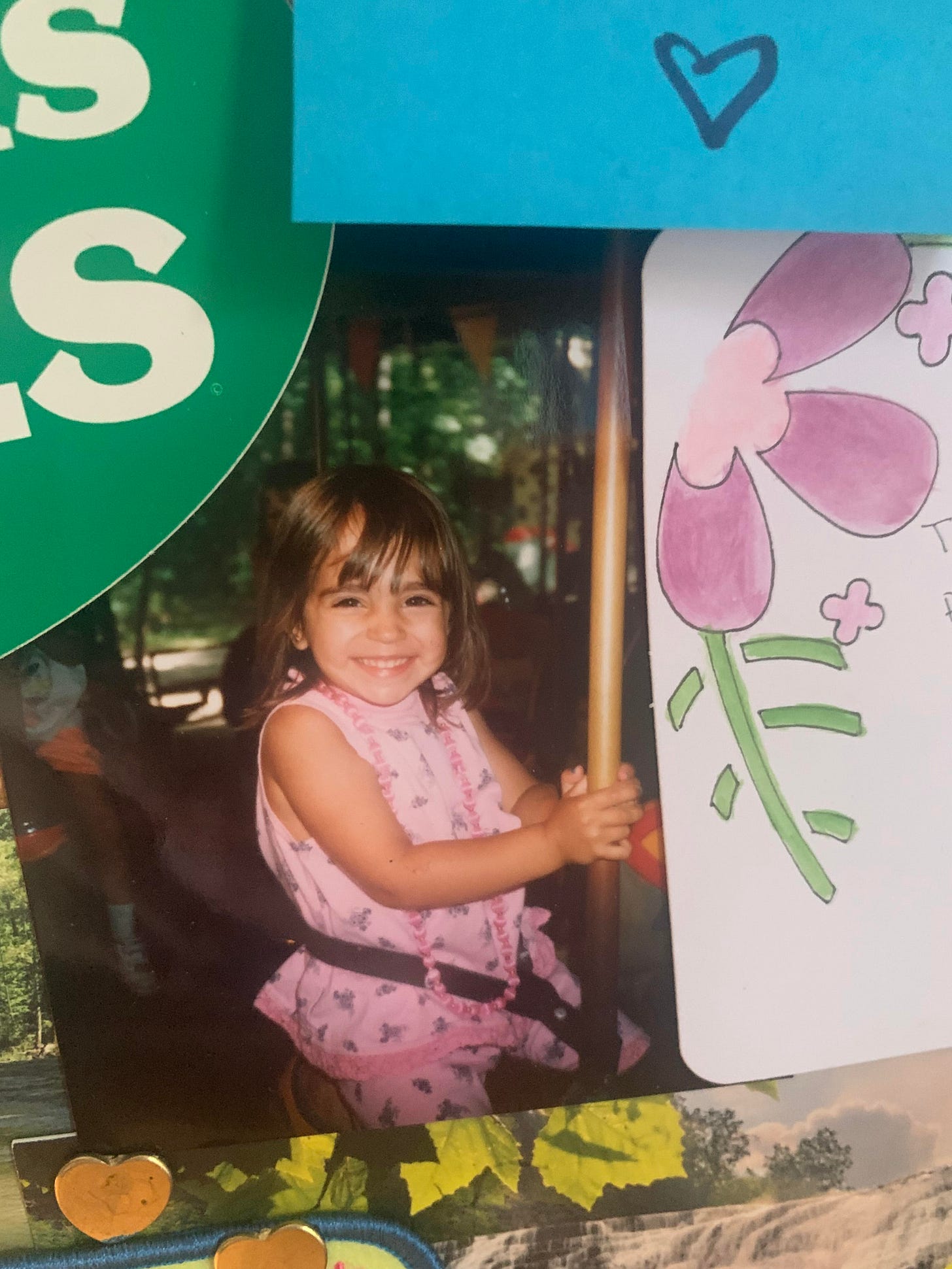 A picture of a photo pinned to a cork board. In it, the writer as a small child with brown hair in a bob sits on a carousel horse and she is smiling A picture of a photo pinned to a cork board. In it, the writer as a small child with brown hair in a bob sits on a carousel horse and she is smiling