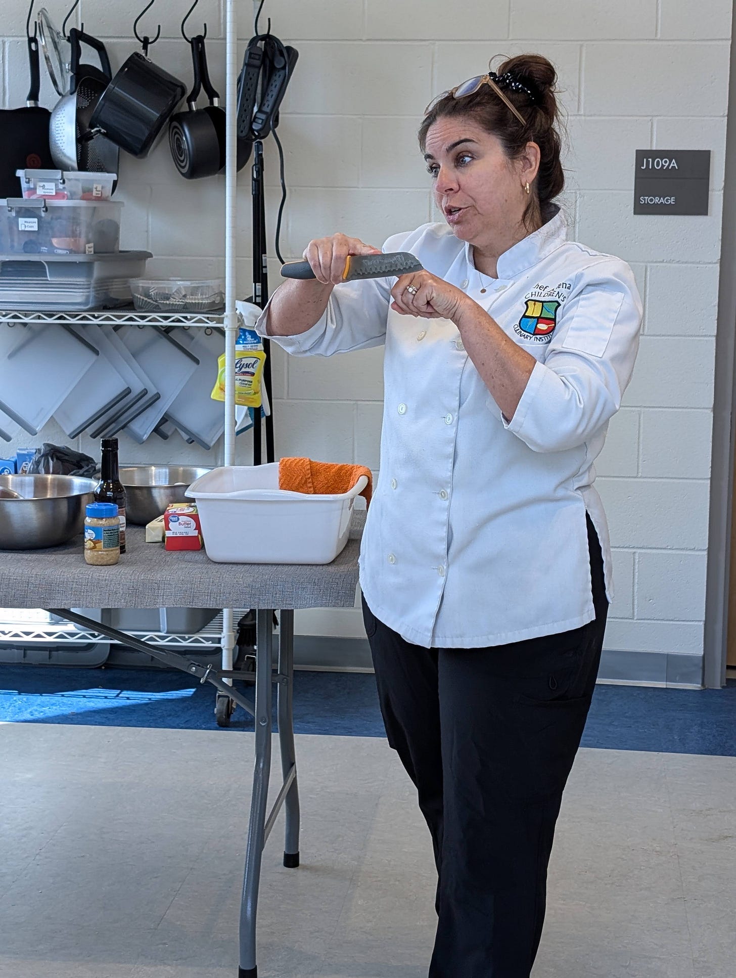 chef in white coat standing a demonstrating knife skills 