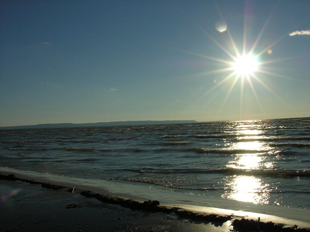 Low sun over the horizon at Wasaga Beach casting a long reflection across the waves and darkened shoreline. Low sun over the horizon at Wasaga Beach casting a long reflection across the waves and darkened shoreline.