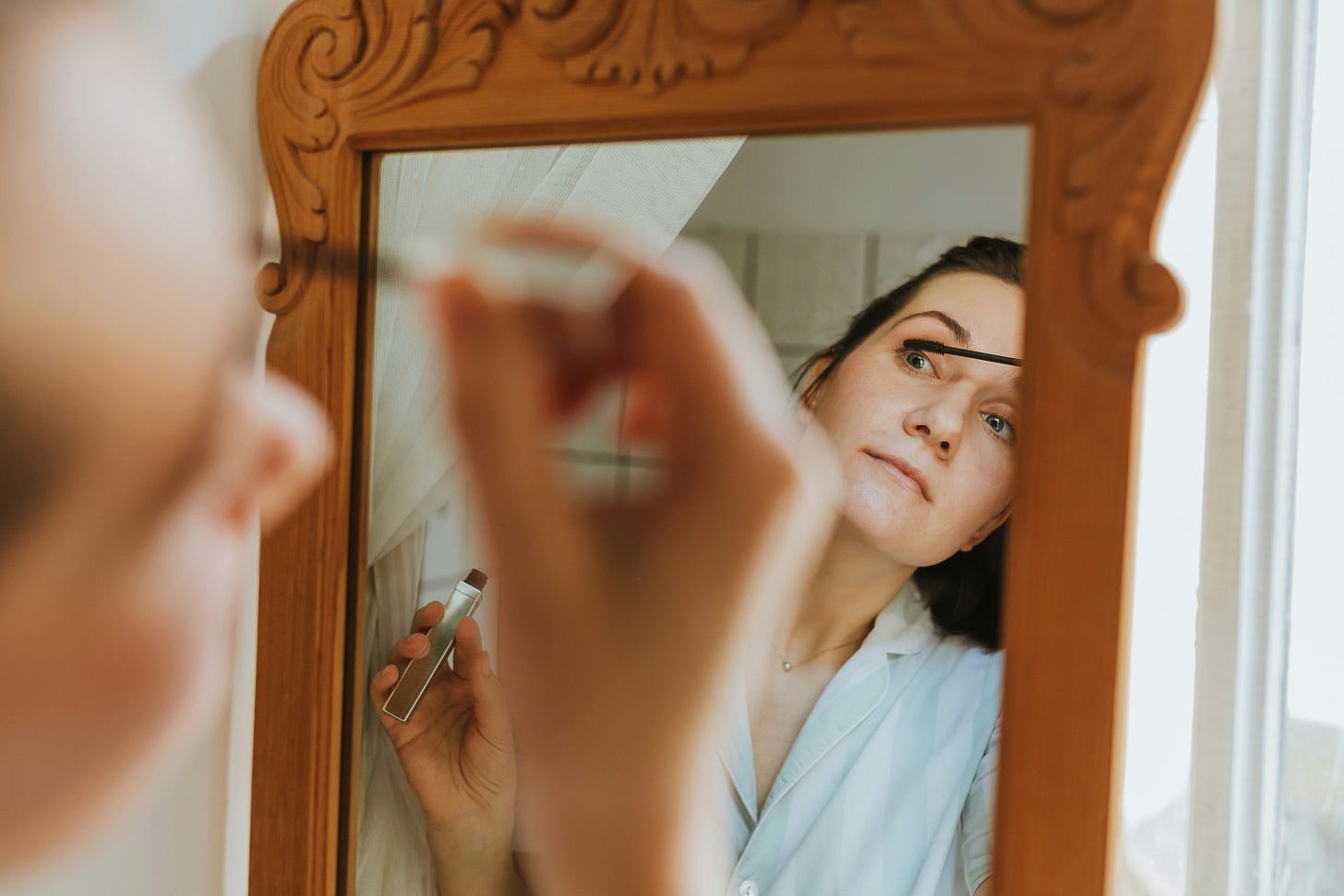 A woman puts on makeup while looking in a mirror. 