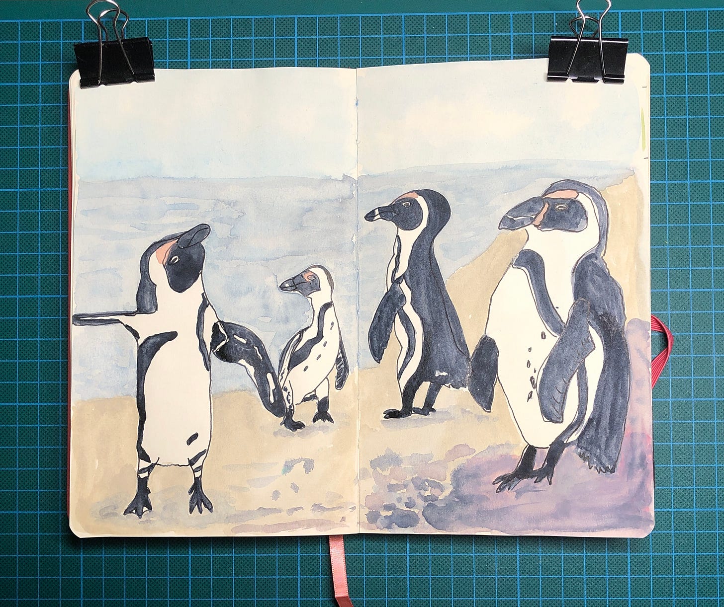 Photo d'une double-page de mon sketchbook où j'ai peint 4 pingouins sur une plage. Photo d'une double-page de mon sketchbook où j'ai peint 4 pingouins sur une plage.
