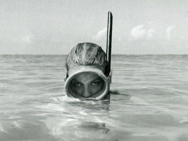 This may contain: an old photo of a woman in the water with a scuba mask on her head