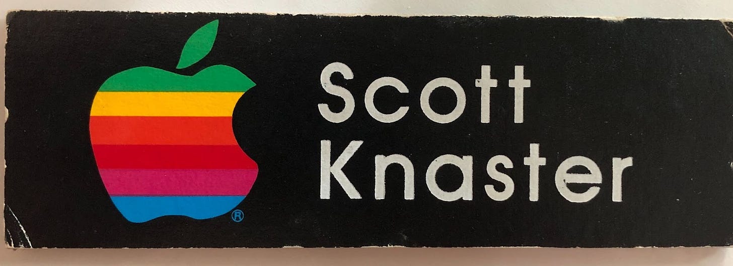 The author's office nameplate at work reads "Scott Knaster" and has the old six-color Apple logo. The edges of the logo appear sloppy and misshapen.