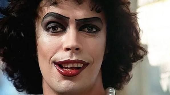Close-up of a smiling person with curly dark hair, dramatically arched black eyebrows, heavy eye makeup and dark red lipstick. Close-up of a smiling person with curly dark hair, dramatically arched black eyebrows, heavy eye makeup and dark red lipstick.