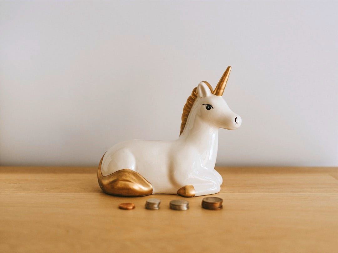 white and gold ceramic unicorn figurine near coins white and gold ceramic unicorn figurine near coins