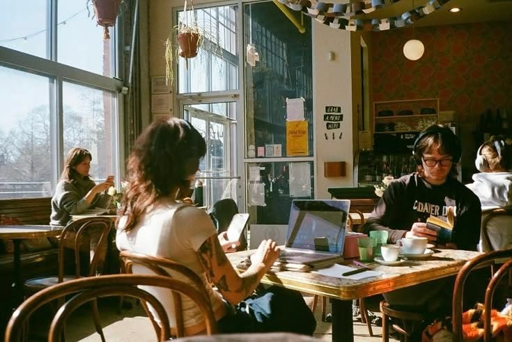 This may contain: people sitting at tables in a restaurant with laptops and coffee cups on the table