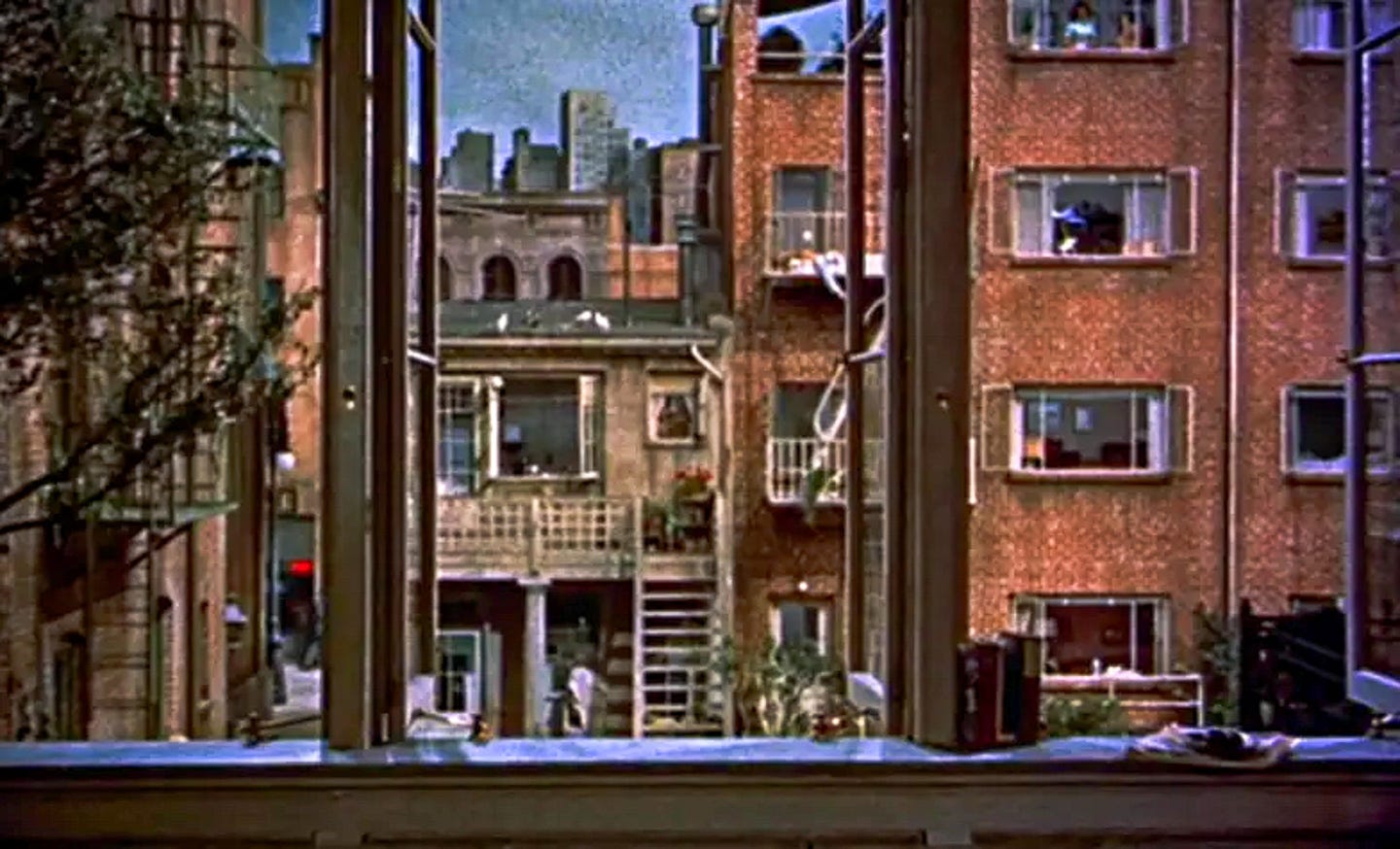 A view through an open window into a 1950s brick apartment courtyard, framed by buildings and fire escapes, from Alfred Hitchcock’s Rear Window (1954). A view through an open window into a 1950s brick apartment courtyard, framed by buildings and fire escapes, from Alfred Hitchcock’s Rear Window (1954).