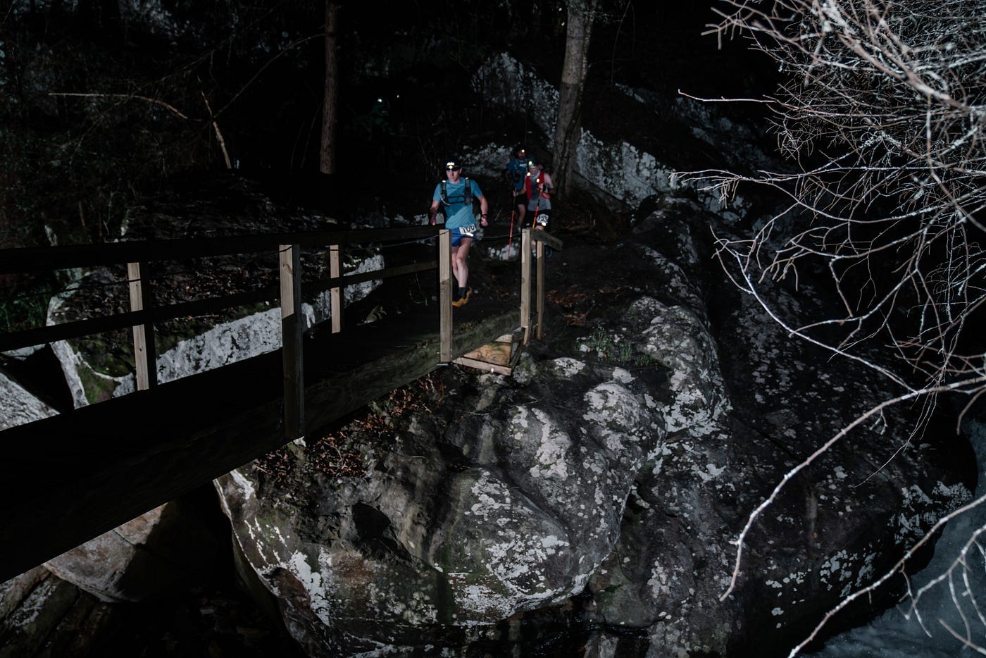A group of people running over a narrow foot bridge at night.