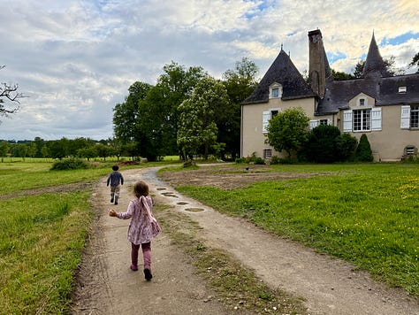An overhead garden table with bread, cheese, carrots, apples, grapes and drinks; two children eating at a white bistro table with the château behind; two children running down a path toward the château.