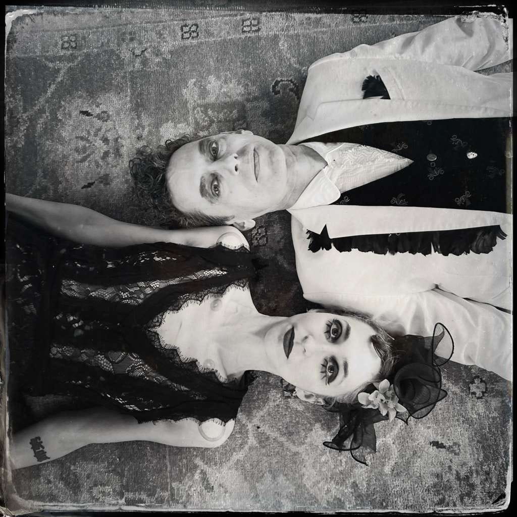 Black-and-white portrait of gothic folk duo Charming Disaster lying side by side on a patterned rug, photographed for their Tarot DMs interview. Black-and-white portrait of gothic folk duo Charming Disaster lying side by side on a patterned rug, photographed for their Tarot DMs interview.