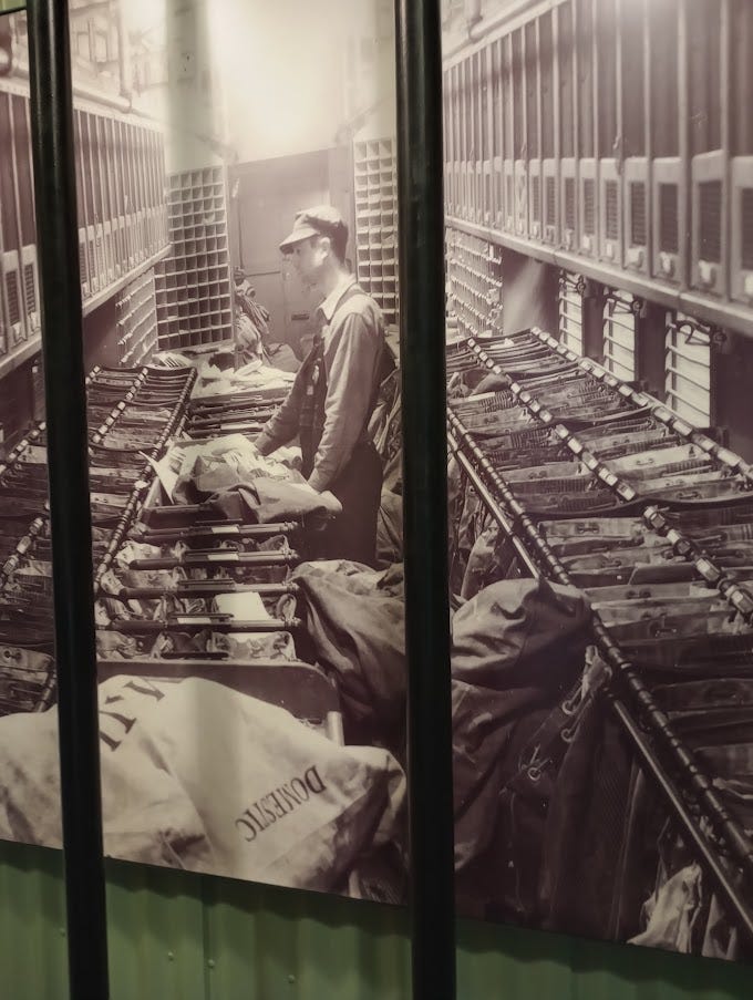 Photo of man in early 20th century sorting mail on train, mailbags and slots on mail train carriage in museum. Mail catcher used by moving train