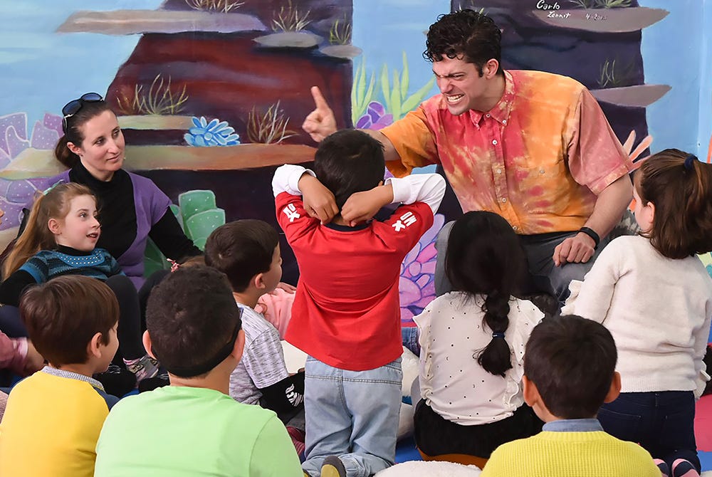 Chip telling stories to a group of small and smiling children at a library
