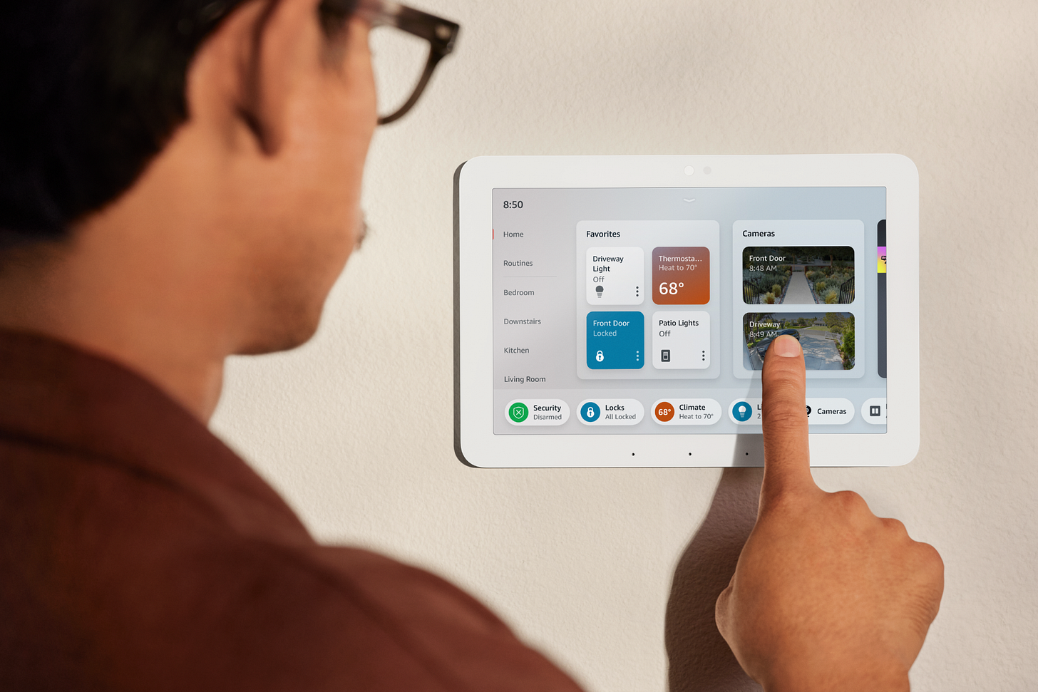 An over-the-shoulder view of a person wearing eyeglasses tapping on a wall-mounted Amazon Echo Hub.
