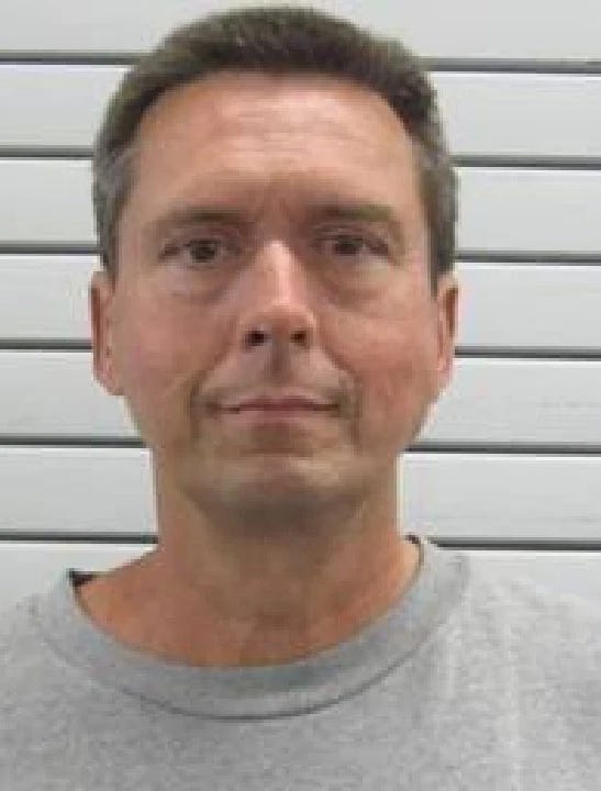 Mugshot of a man with short brown hair wearing a gray t-shirt.