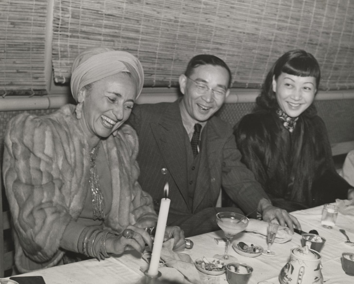 Bernardine Fritz in furs and turban and jewels, Lin Yutang in between her and AMW also wearing a dark fur coat, sitting at a dinner table and laughing together Bernardine Fritz in furs and turban and jewels, Lin Yutang in between her and AMW also wearing a dark fur coat, sitting at a dinner table and laughing together