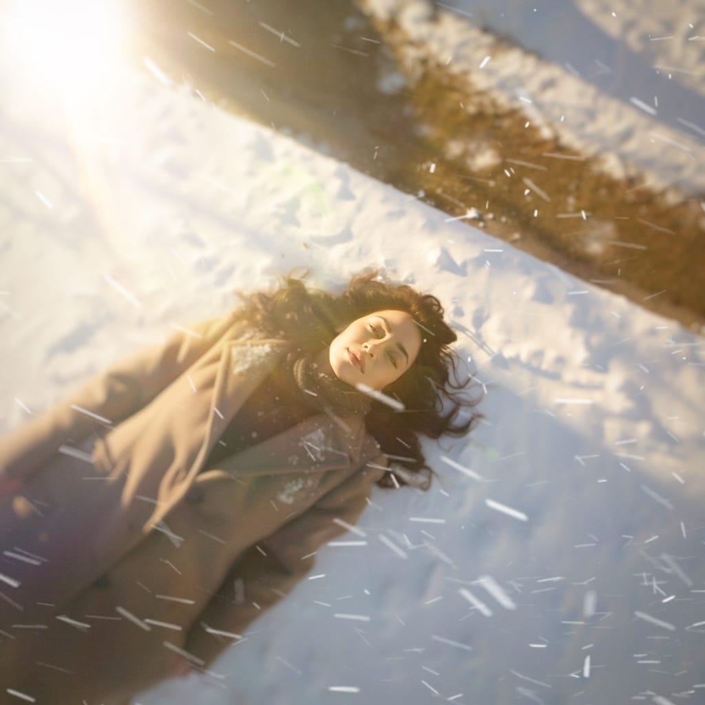 An unconscious woman lays on the ground while snow falls around her.