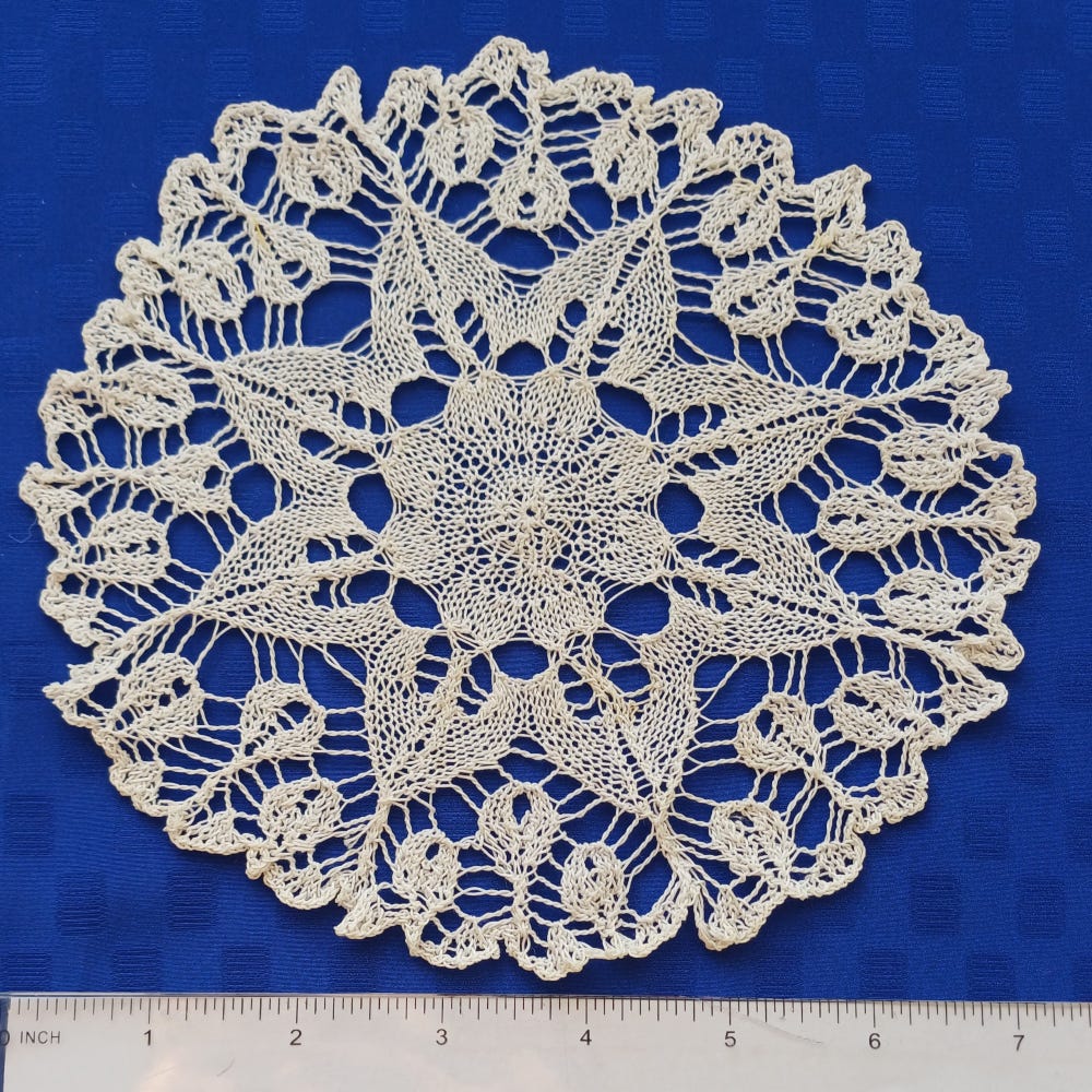 White doily against blue background, with scale showing how delicate the work is