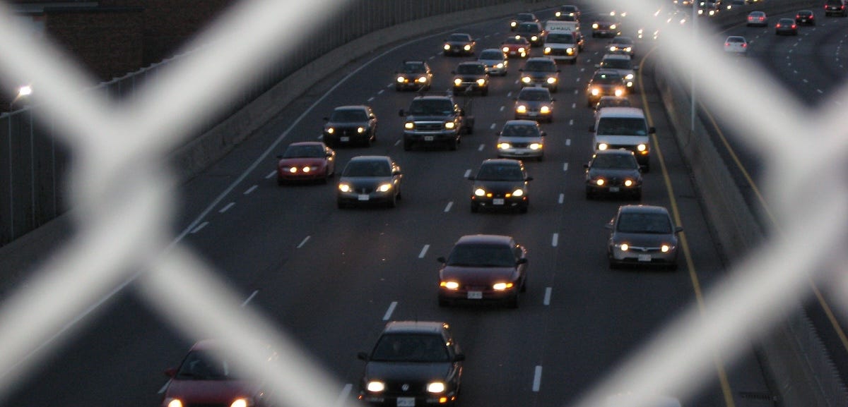 four lanes of oncoming traffic with headlights on at dusk. photographed through a chink in a chain-link fence. four lanes of oncoming traffic with headlights on at dusk. photographed through a chink in a chain-link fence.