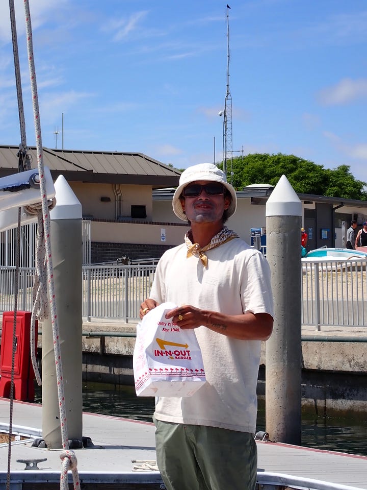 Working on the lashing for the back of the canoe on the water, using a trigger gun to apply quick dry marine crack repair to exposed wood on the boat, chris eating in n out with a big smile, our teak wood center board in place on ʻAʻĀ