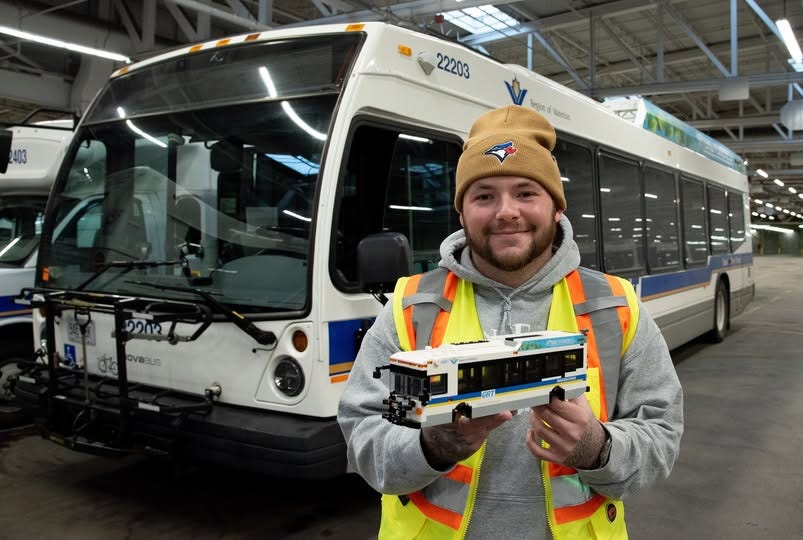Man standing in front of a GRT bus holding a Lego imitation of a GRT bus.
