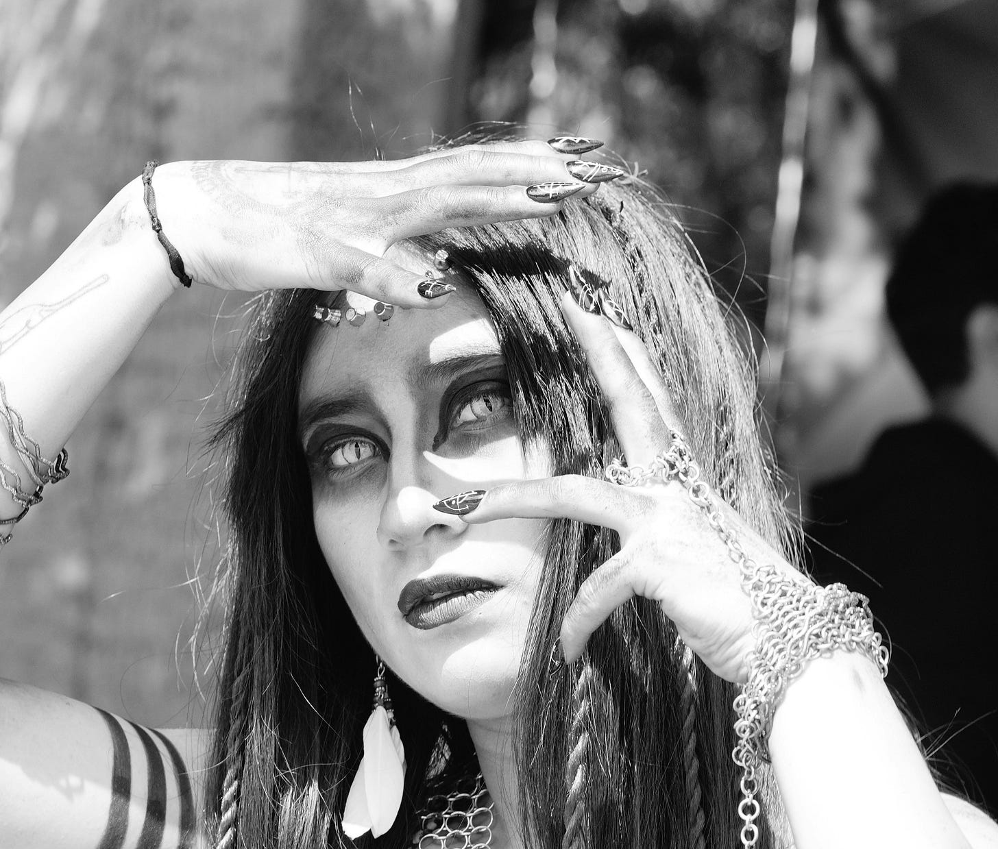 Black-and-white close-up of a woman with long dark hair and ornate jewelry, framing her face with her hands and staring intensely. Black-and-white close-up of a woman with long dark hair and ornate jewelry, framing her face with her hands and staring intensely.