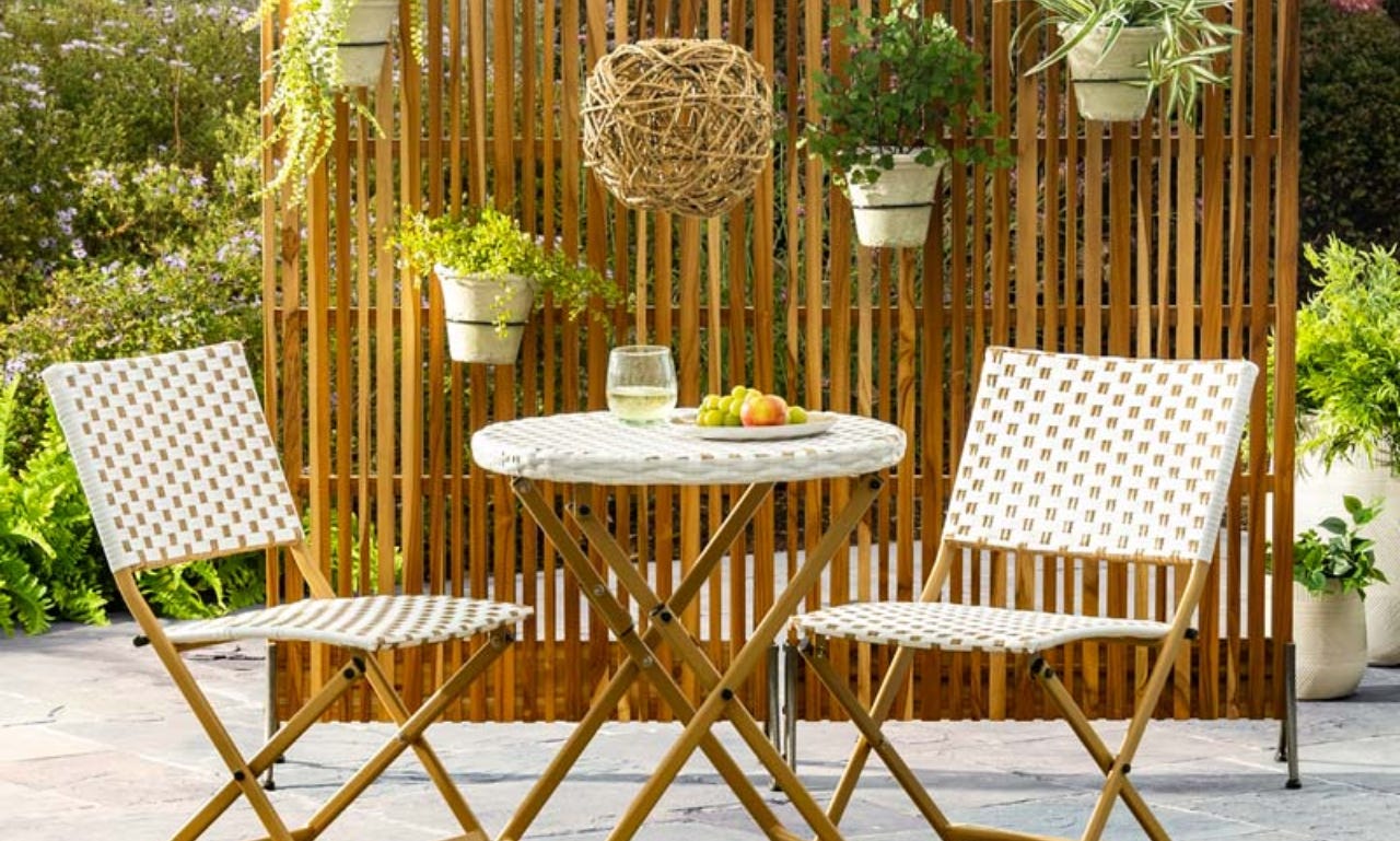two chairs and a patio table in front of a teak partition with plants hanging from it