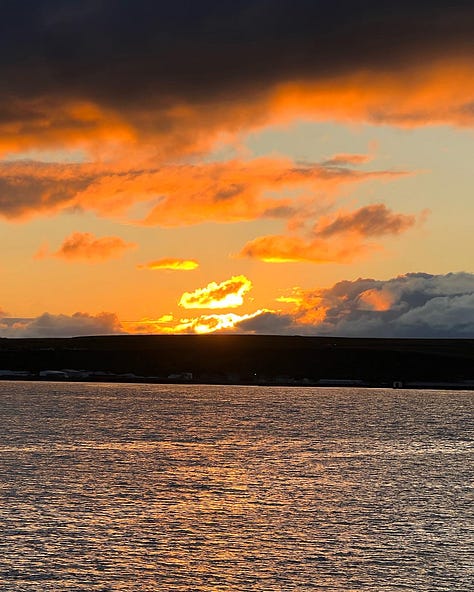 Jem and Jack, in cycle helmets stand in front of the John O'Groats sign. A picture of a highland cow, and a firey sunset about the sea burns with a bright orang